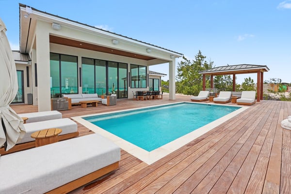 Modern house with rectangular swimming pool, wooden deck, lounge chairs, and pergola overlooking desert landscape
