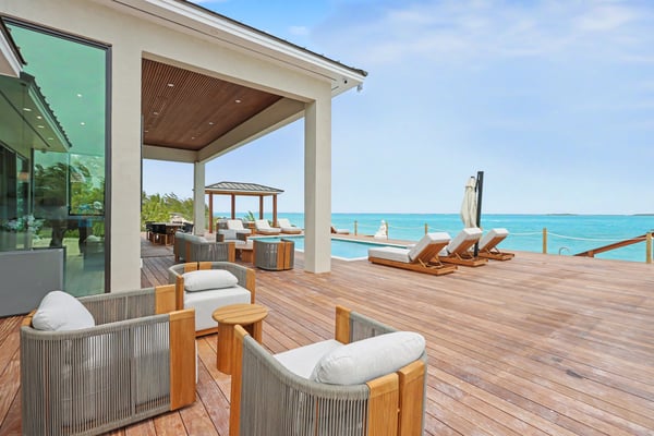 Beachfront deck with lounge chairs, wooden furniture, pergola, and turquoise ocean view