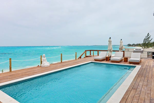 Waterfront deck with swimming pool, lounge chairs, umbrellas, and turquoise ocean view