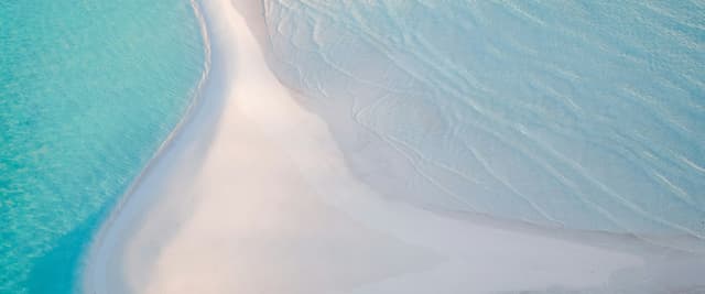 Aerial view of an Exuma sandbar at sunrise, pale blue water curving around white sand